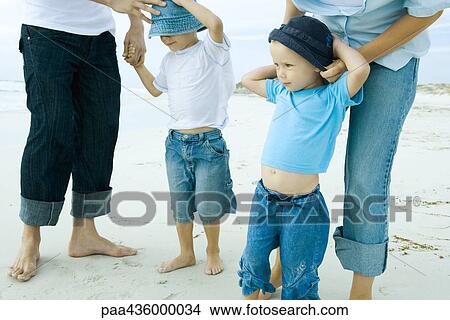 Picture - Parents putting sunhats on children at the beach, low section. Fotosearch
