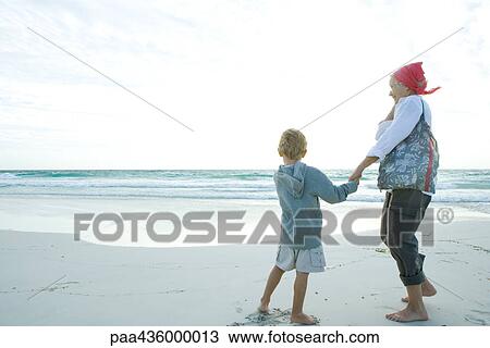 Stock Image - Senior woman standing on beach with grandson. Fotosearch