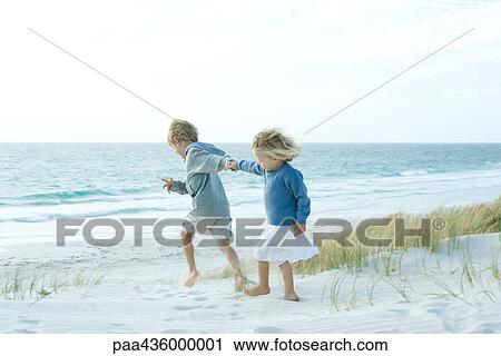 Stock Image - Sister and brother holding hands on beach. Fotosearch