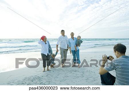Stock Image - Three generation family on beach, mid adult man taking group photo. Fotosearch