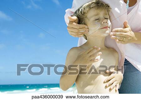Stock Photo - Woman applying sunscreen to son's face on beach. Fotosearch