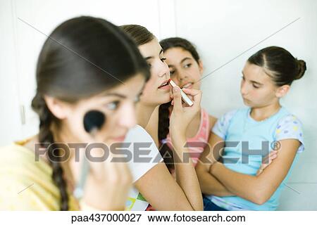 Stock Photo - Four young female friends putting on make-up. Fotosearch