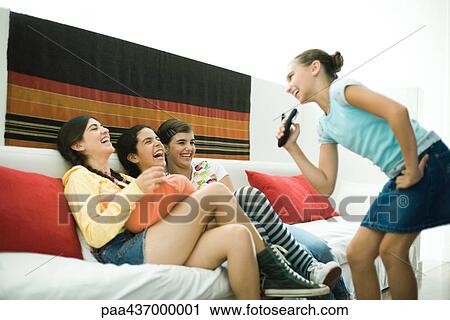 Stock Image - Preteen girl singing into remote control, friends laughing. Fotosearch