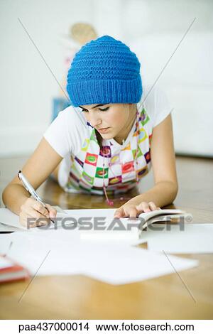 Picture - Teen girl lying on floor, doing homework. Fotosearch