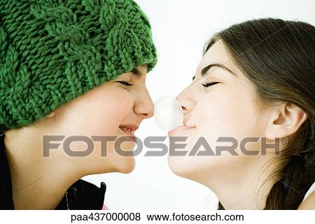 Stock Photo - Two young female friends, one blowing bubble with gum, touching friend's nose. Fotosearch
