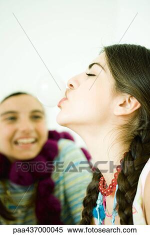 Stock Photography - Two young female friends, one blowing bubble with chewing gum. Fotosearch