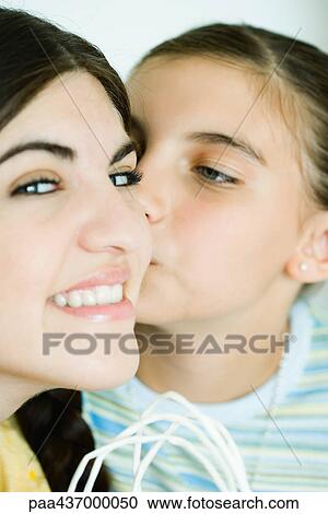 Stock Image - Two young female friends, one kissing the other on the cheek. Fotosearch