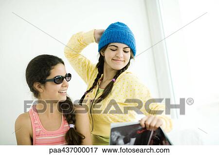Stock Photo - Two young female friends, one looking at magazine and posing. Fotosearch