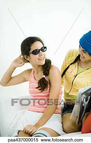 Stock Photography - Two young female friends, one wearing sunglasses and holding hand behind head. Fotosearch