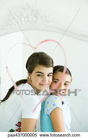 Stock Photography - Two young female friends, reflected in mirror with heart drawn in lipstick. Fotosearch