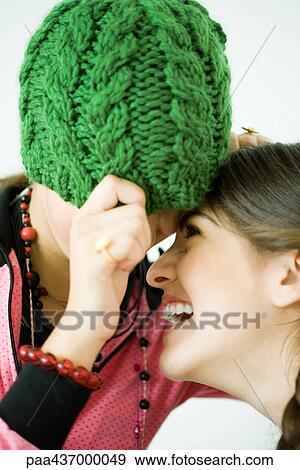 Stock Photo - Two young female friends with heads together, one pulling knit hat over eyes while the other laughs. Fotosearch