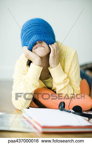 Stock Photograph - Young woman lying on floor, pulling knit hat down over eyes. Fotosearch