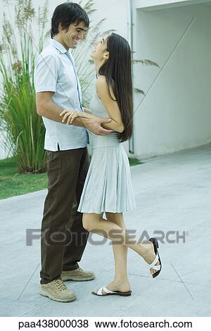 Stock Photo - Couple standing holding each other's arms, laughing, full length. Fotosearch