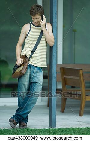Man leaning on pole, using cell phone, full length View Large Photo Image Stock Photo - Man leaning on pole, using cell phone, full length. Fotosearch