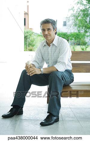 Man sitting on patio holding glass of champagne, full length View Large Photo Image Picture - Man sitting on patio holding glass of champagne, full length. Fotosearch