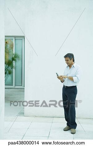 Man standing looking at cell phone, full length View Large Photo Image Picture - Man standing looking at cell phone, full length. Fotosearch