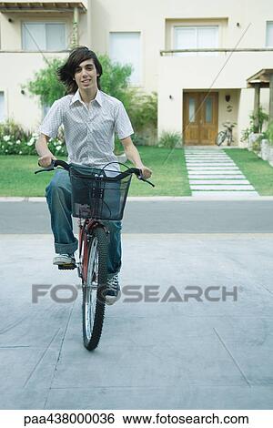 Stock Photograph - Teen boy riding bicycle in residential neighborhood, full length. Fotosearch