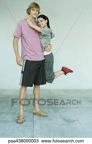 Stock Image - Teen girl hanging from boyfriend's neck, full length. Fotosearch