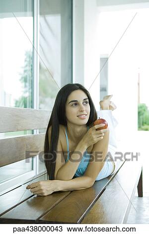 Woman lying on stomach on bench, holding apple, full length View Large Photo Image Stock Image - Woman lying on stomach on bench, holding apple, full length. Fotosearch