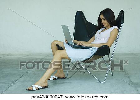 Woman sitting in chair using laptop, full length View Large Photo Image Stock Photo - Woman sitting in chair using laptop, full length. Fotosearch