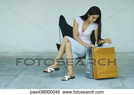 Woman sitting, looking in shopping bags, full length View Large Photo Image Stock Photograph - Woman sitting, looking in shopping bags, full length. Fotosearch