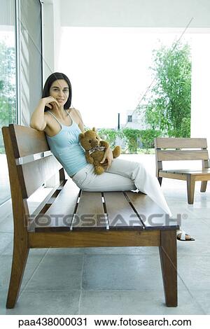Woman sitting on patio furniture holding teddy bear, full length View Large Photo Image Stock Image - Woman sitting on patio furniture holding teddy bear, full length. Fotosearch