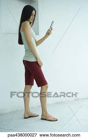 Woman standing, looking at cell phone, full length View Large Photo Image Stock Photo - Woman standing, looking at cell phone, full length. Fotosearch