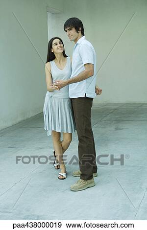 Stock Photo - Young couple standing holding hands, full length. Fotosearch
