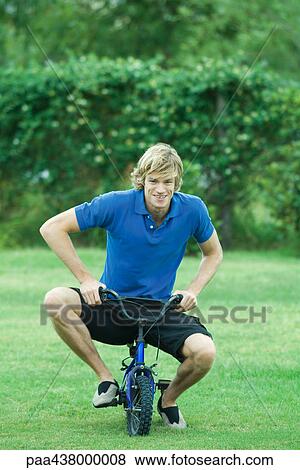 Young man riding child's bike, full length View Large Photo Image Stock Photo - Young man riding child's bike, full length. Fotosearch