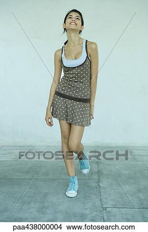 Young woman standing with one foot off the ground, looking up, full length View Large Photo Image Picture - Young woman standing with one foot off the ground, looking up, full length. Fotosearch