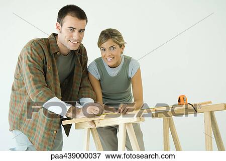 Couple leaning on sawhorses, using measuring tape, smiling at camera View Large Photo Image Stock Photo - Couple leaning on sawhorses, using measuring tape, smiling at camera. Fotosearch