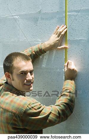 Man measuring wall with measuring tape, smiling over shoulder at camera View Large Photo Image Stock Photo - Man measuring wall with measuring tape, smiling over shoulder at camera. Fotosearch