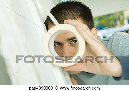 Man putting masking tape on surface, looking through hole View Large Photo Image Stock Image - Man putting masking tape on surface, looking through hole. Fotosearch