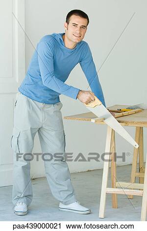 Man sawing piece of wood, looking at camera View Large Photo Image Stock Image - Man sawing piece of wood, looking at camera. Fotosearch