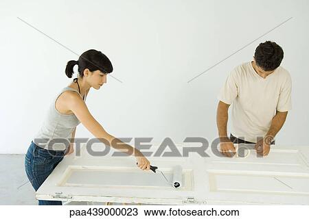 Stock Image - Woman painting door while man applies masking tape. Fotosearch