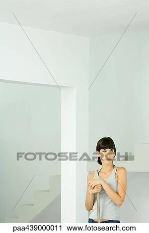 Stock Image - Woman standing in bare home interior, resting hands on wooden pole. Fotosearch