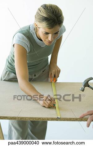 Stock Image - Woman using measuring tape to draw line on wood board. Fotosearch