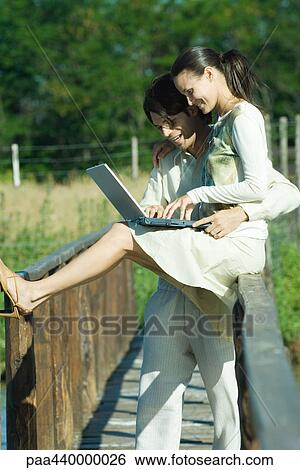Couple on footbridge using laptop View Large Photo Image Stock Photograph - Couple on footbridge using laptop. Fotosearch