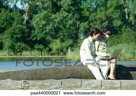Couple sitting by water, using laptop View Large Photo Image Stock Image - Couple sitting by water, using laptop. Fotosearch