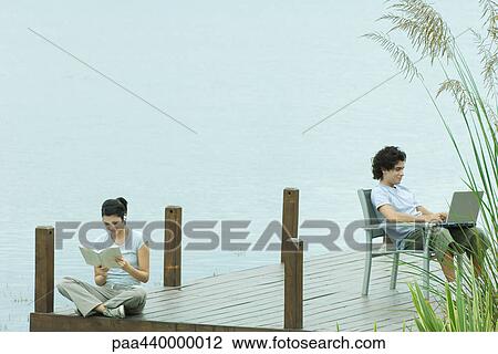 Couple sitting on dock, reading and using laptop View Large Photo Image Stock Image - Couple sitting on dock, reading and using laptop. Fotosearch