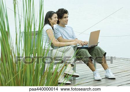 Couple sitting on dock using laptop View Large Photo Image Picture - Couple sitting on dock using laptop. Fotosearch