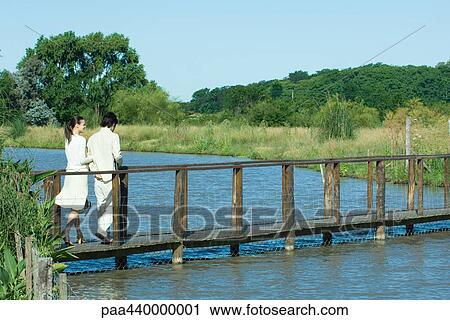 Stock Image - Couple walking over river on footbridge. Fotosearch