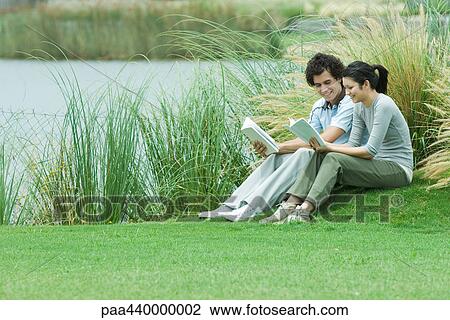 Young adult couple reading outdoors, sitting on grass by edge of lake View Large Photo Image Stock Image - Young adult couple reading outdoors, sitting on grass by edge of lake. Fotosearch