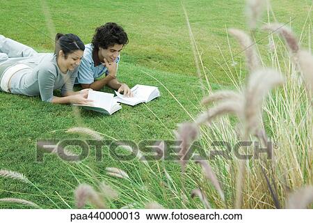 Young adult couple reading outdoors, lying on grass View Large Photo Image Stock Image - Young adult couple reading outdoors, lying on grass. Fotosearch