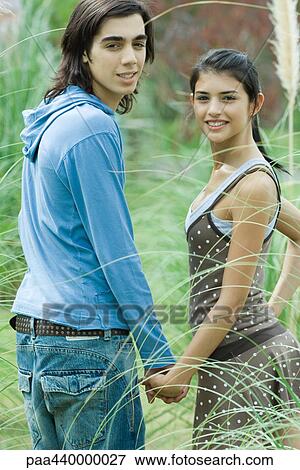 Young couple holding hands, looking over shoulders at camera View Large Photo Image Stock Photo - Young couple holding hands, looking over shoulders at camera. Fotosearch