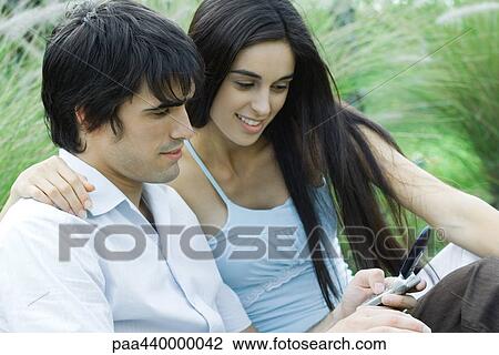 Young couple outdoors together, looking at cell phone View Large Photo Image Stock Image - Young couple outdoors together, looking at cell phone. Fotosearch