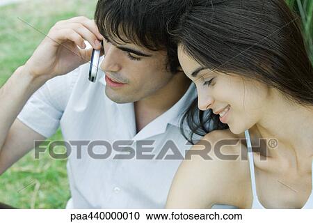 Young couple sitting close together, man using cell phone View Large Photo Image Stock Image - Young couple sitting close together, man using cell phone. Fotosearch