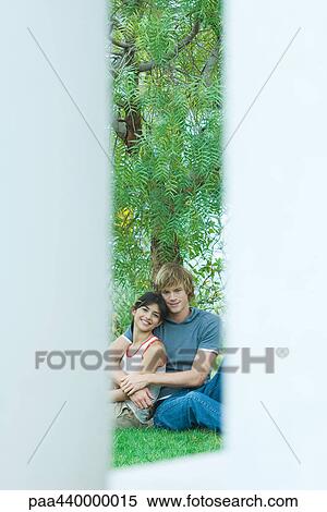 Young couple sitting on ground, leaning against tree, smiling at camera View Large Photo Image Stock Photography - Young couple sitting on ground, leaning against tree, smiling at camera. Fotosearch
