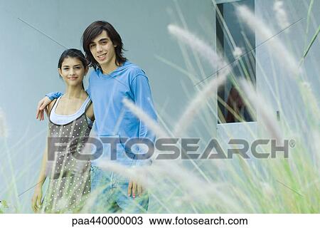 Stock Image - Young couple, smiling at camera, long grass in foreground. Fotosearch