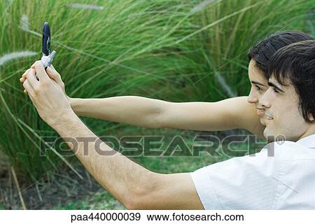 Stock Photo - Young couple taking photo of selves with cell phone. Fotosearch